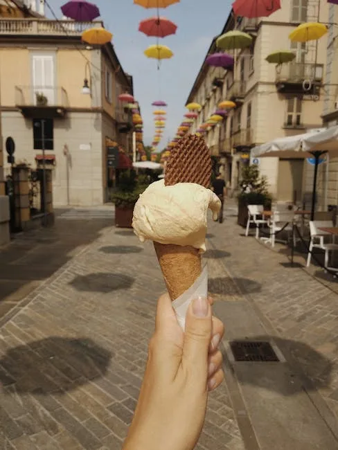 Hand houdt ijsje vast op straat met zwevende paraplu's in Cinque Terre
