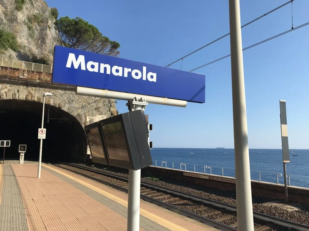 Pancarte 'Manarola' sur le quai du train face à la mer.