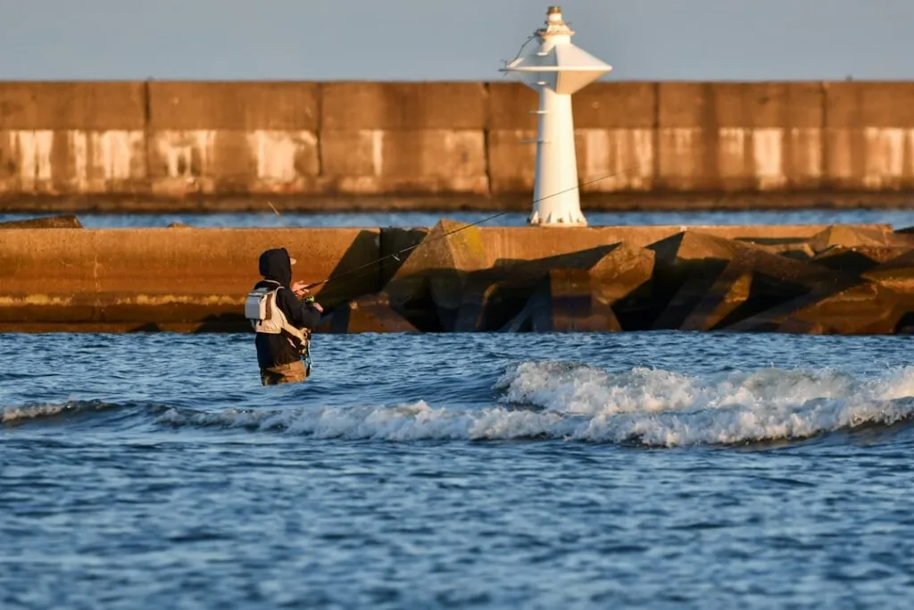 Pêcheur en waders dans la mer devant un môle et une balise