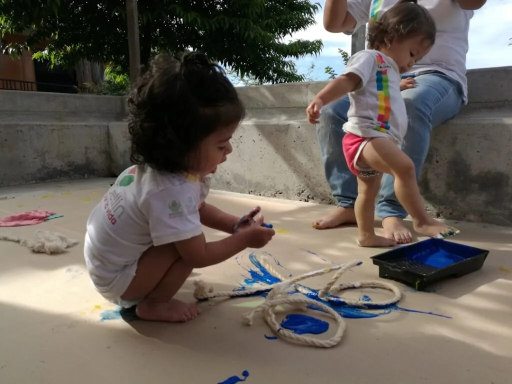 Deux jeunes enfants peignent à même le sol avec peinture bleue
