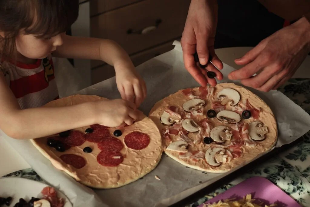 Enfant et adulte déposent olives et champignons sur pizzas crues