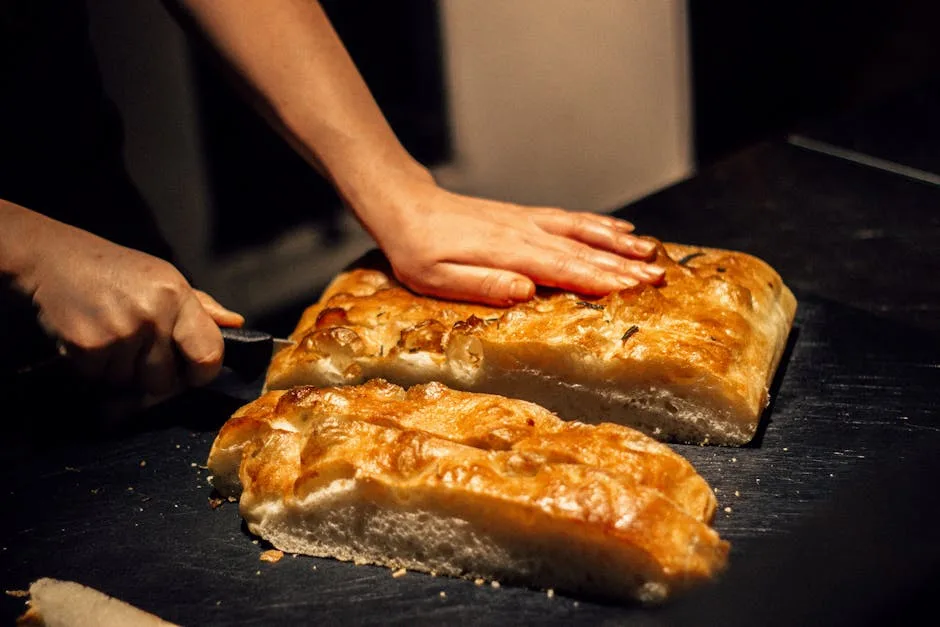 Mains tranchant une focaccia dorée, pain artisanal prêt à servir
