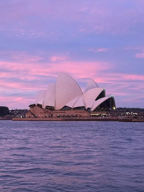 Opéra de Sydney éclairé au crépuscule, ciel rose et eaux calmes