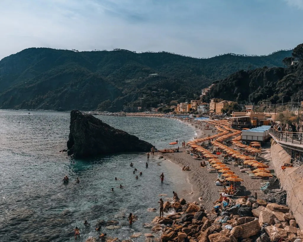 Grande plage des Cinque Terre bordée de parasols orange et rocher.